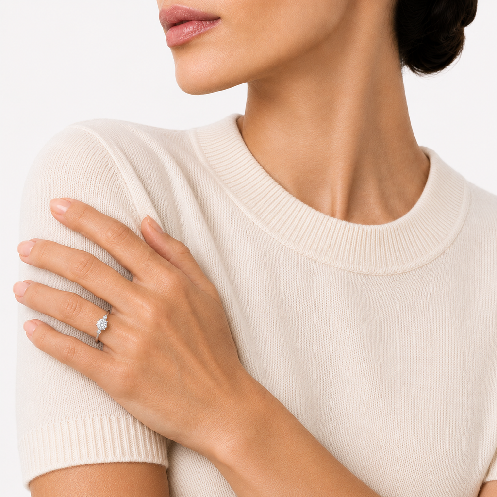 A model wearing a trio ring with a round brilliant cut moissanite weighing 1ct flanked by two smaller stones, white gold plated sterling silver